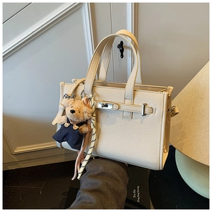 Detail of creamy white litchi grain leather tote with metal turn-lock and cute bear charm