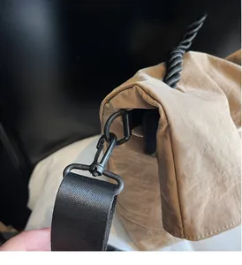 Detail of khaki nylon bag featuring black metal swivel hooks and a wide woven strap
