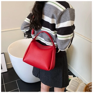 Red pebbled leather handbag with curved handle and detachable strap worn by a model
