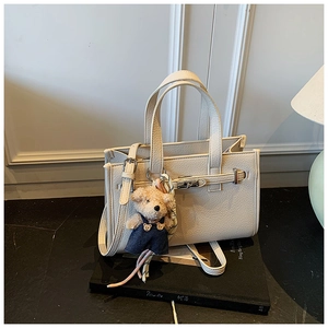 Detail of cream white pebbled leather bag with metal turn-lock and brown bear charm