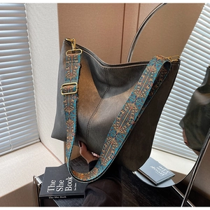 Detail of grey leather bucket bag featuring a colorful bohemian style woven shoulder strap