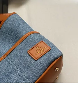 Détail de denim bleu et cuir marron avec rivets métalliques sur un sac seau