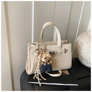 Detail of off-white lychee texture faux leather handbag with cute bear charm on books