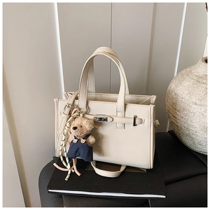 Detail of off-white lychee grain tote bag with silver turn-lock and cute teddy bear charm