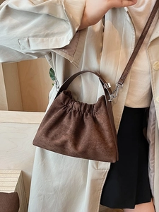Sac nuage plissé en daim marron foncé avec bandoulière porté sur un manteau beige
