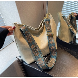 Close-up of beige suede tote bag featuring a colorful Bohemian style woven shoulder strap