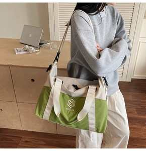 Green and beige travel bag with adjustable strap worn by model in a modern office setup