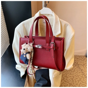 Detail of red pebbled leather mini square bag with metal buckle and plush bear charm