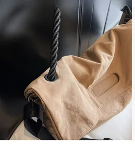 Detail of khaki nylon tote bag featuring industrial black rope handles and metal eyelets