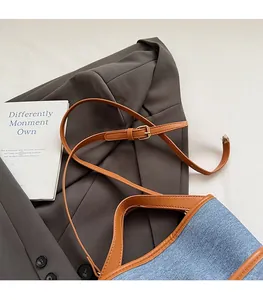 Vue à plat d'un sac seau en denim bleu avec lanières en cuir marron sur un blazer gris