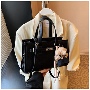 Detail of black lychee leather handbag with silver lock and brown plush bear charm