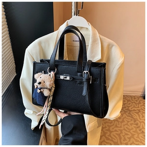 Detail of black lychee grain leather handbag with rotating lock and bear charm accessory