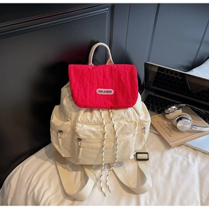 Detail of a white nylon backpack with a red contrast flap, drawstring, and multiple pockets