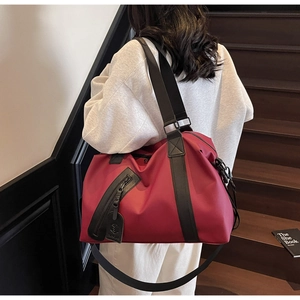 Detail of burgundy nylon travel bag with wide black strap on wooden stairs in a home setting
