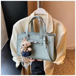 Detail of light blue lychee pattern handbag with metal turn-lock and cute bear charm