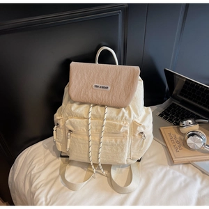 Detail of cream-white nylon backpack featuring drawstring closure and textured flap