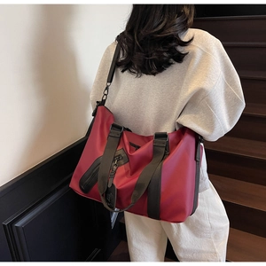 Deep red travel tote bag with black straps shown in a modern lifestyle setting