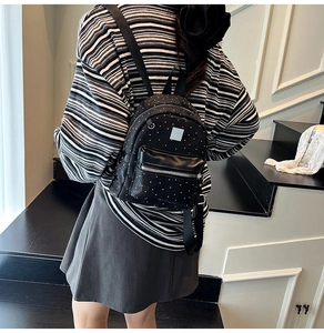 Detail of a mini black backpack with white polka dots on a model in casual setting