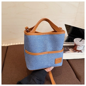 Détail du sac seau en denim bleu avec garniture en cuir marron et logo sur une table