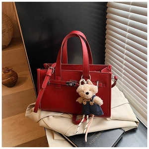 Detail of red litchi leather handbag with metal twist lock and a cute teddy bear charm