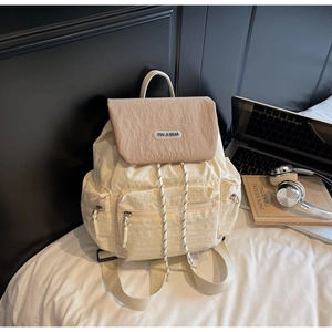 Detail view of cream backpack with brown flap, multiple pockets, and decorative drawstrings