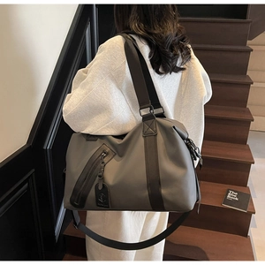 Charcoal grey large capacity travel bag worn by a model on wooden stairs