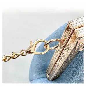 Detail of light gold lobster clasp with flat metal chain and textured bag surface