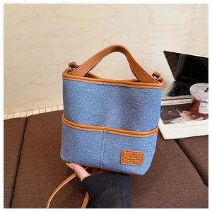 Détail d'un sac seau en denim bleu avec garniture en cuir marron sur bois