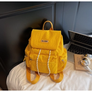 Detail of yellow nylon backpack featuring flap cover and black and white drawstring closure