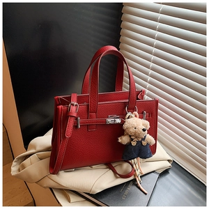 Close-up of red lychee pattern leather handbag with silver clasp and bear charm