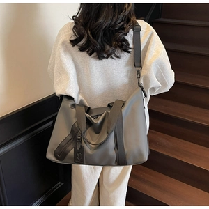 Detail view of a large gray travel duffle bag carried by a person on wooden stairs