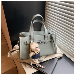 Detail of light green faux leather handbag with silver lock and cute bear keychain