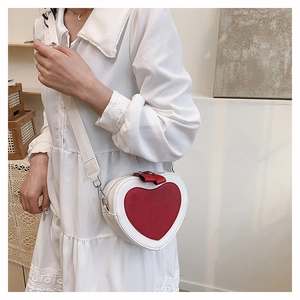 Detail view of heart-shaped crossbody bag with red bow and adjustable wide strap