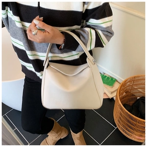 Close-up of beige lychee grain leather handbag with integrated handle in a cozy setting