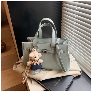Detail of mint green faux leather handbag with silver twist lock and bear charm accessory