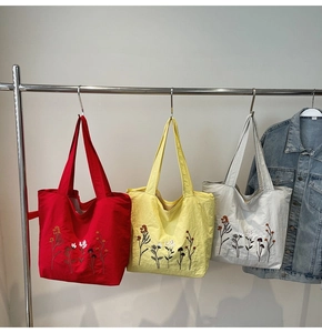 Detailed view of red, yellow and grey canvas tote bags with colorful flower embroidery