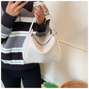 Detail shot of ivory pebble leather texture and minimalist curved handle on women's bag