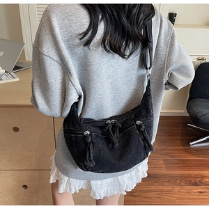 Detail view of a black denim moon-shaped crossbody bag worn over a gray sweatshirt