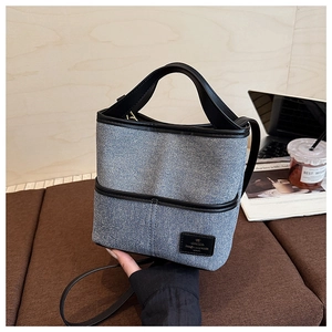 Détail du sac seau en denim bleu avec finitions en cuir noir dans un café cosy