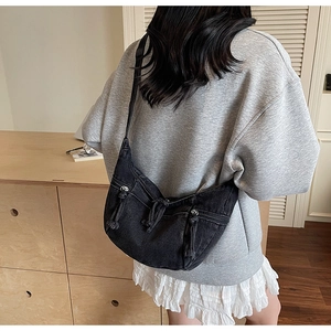 Detail view of a black denim moon-shaped crossbody bag with tassels worn by a model