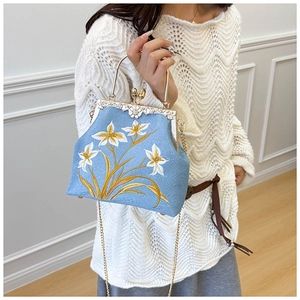 Close-up of light blue silk embroidery bag with floral patterns and gold chain