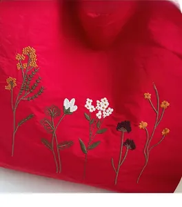 Close-up of fine floral embroidery on the red fabric of a large canvas tote bag