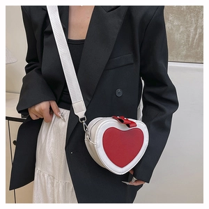 Detail of white heart-shaped crossbody bag with red contrast heart on black suit