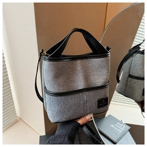 Détail du sac seau en denim bleu avec garniture en cuir noir tenu à la main dans un décor