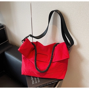 Detail of red large capacity crossbody bag with wide strap on a leather sofa