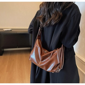 Detail of dark brown leather crescent bag with adjustable strap and side buckle accents