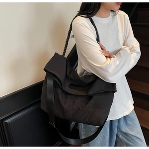 Detail of black canvas crossbody bag featuring woven rope handle and wide nylon strap