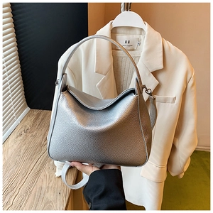Close-up of the silver litchi grain texture and curved handle on a modern handbag