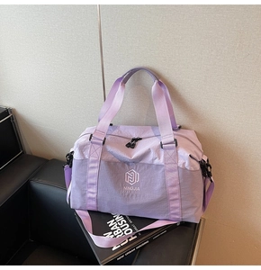 Detail view of purple nylon travel bag with brand embroidery on a leather chair
