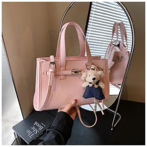 Detailed view of pink pebble grain handbag with metal turn-lock and cute bear charm